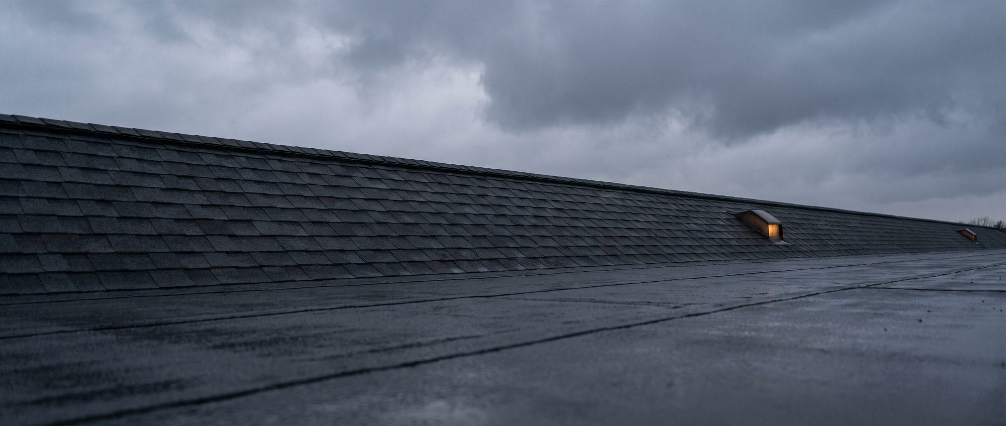 A long run of finished architectural shingle roofline against a clearing storm sky.